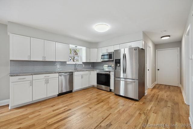 kitchen featuring stainless steel appliances, a sink, backsplash, white cabinets, and light wood-style flooring