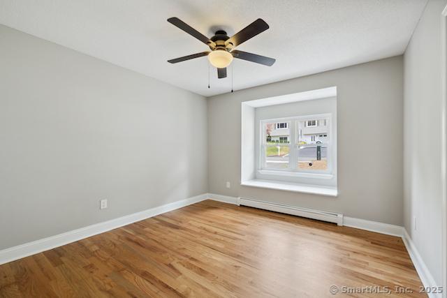 spare room featuring a baseboard heating unit, light wood-style flooring, baseboards, and a ceiling fan
