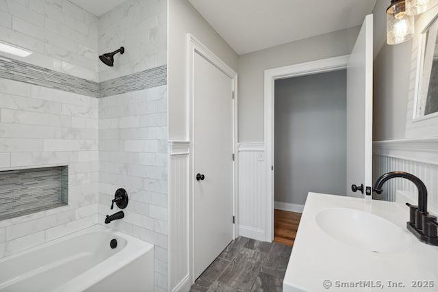 bathroom with tub / shower combination, vanity, and a wainscoted wall