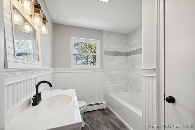 bathroom with a baseboard heating unit, a wainscoted wall, toilet, vanity, and bathtub / shower combination
