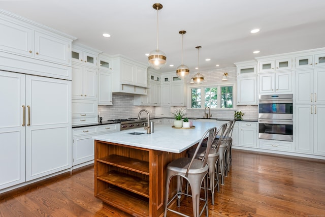 21 Park Pl, Darien, CT 06820 - kitchen featuring stainless steel double oven, backsplash, dark wood-style flooring, a kitchen island with sink, and a kitchen bar