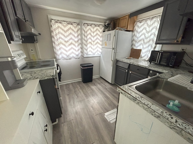 kitchen with white appliances, under cabinet range hood, a sink, and wood finished floors