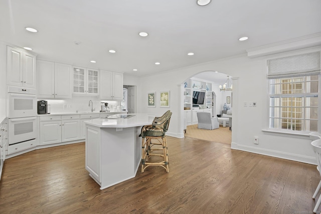 49 Dogwood Ln, New Canaan, CT 06840 - kitchen featuring white double oven, arched walkways, white cabinetry, a breakfast bar area, and light countertops