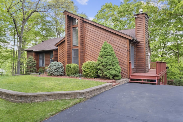 view of home's exterior with a chimney, a lawn, a deck, and a shingled roof