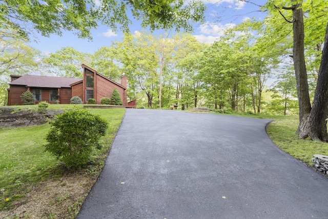 view of property exterior featuring asphalt driveway, a yard, and a chimney