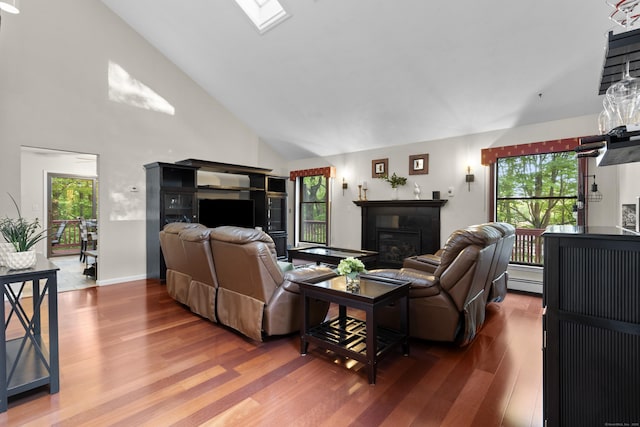 living room with a glass covered fireplace, wood finished floors, high vaulted ceiling, and a baseboard heating unit