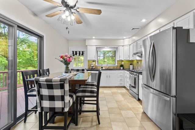 kitchen featuring appliances with stainless steel finishes, under cabinet range hood, dark countertops, tasteful backsplash, and white cabinetry