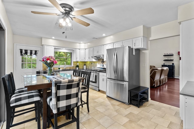 kitchen featuring stainless steel appliances, under cabinet range hood, ceiling fan, white cabinets, and tasteful backsplash
