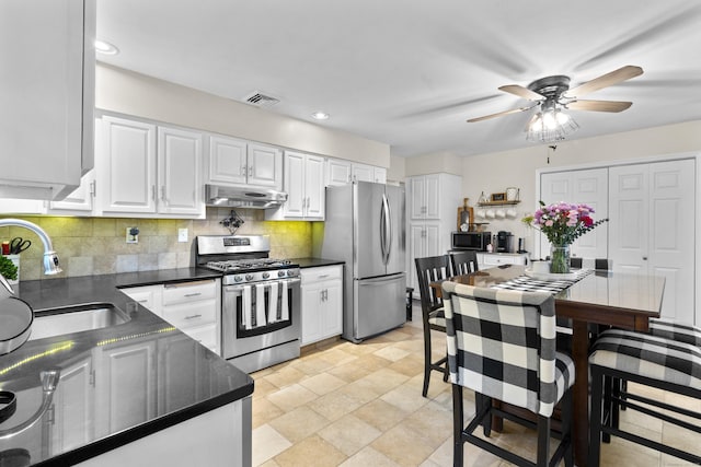kitchen featuring appliances with stainless steel finishes, a sink, under cabinet range hood, dark countertops, and a ceiling fan