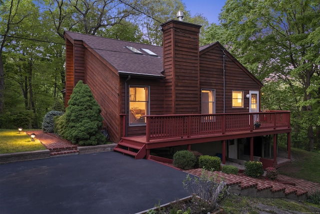 rear view of property with a deck, a shingled roof, a chimney, and a patio area
