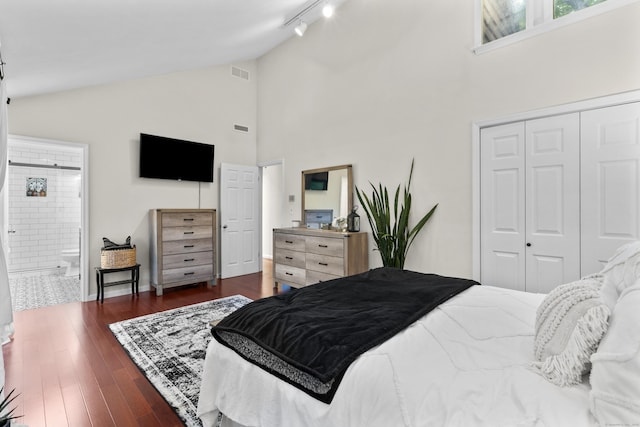 bedroom with a closet, rail lighting, high vaulted ceiling, dark wood finished floors, and connected bathroom