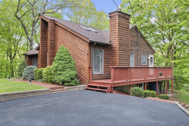 view of side of property featuring a patio, roof with shingles, a wooden deck, and a chimney