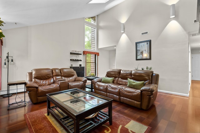 living area featuring a baseboard radiator, a high ceiling, wood finished floors, and baseboards