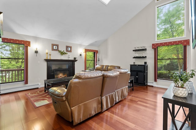 living room with a baseboard heating unit, wood finished floors, a glass covered fireplace, plenty of natural light, and high vaulted ceiling