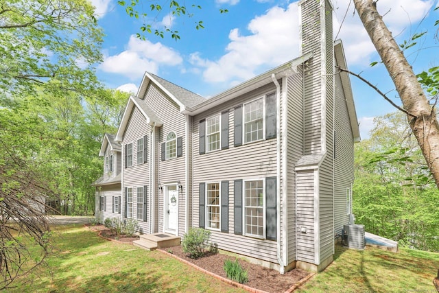 colonial-style house featuring a chimney, central AC, and a front yard
