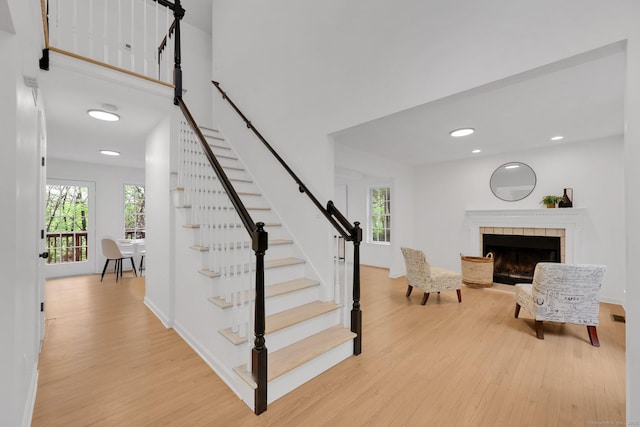 stairway with wood finished floors, healthy amount of natural light, a tile fireplace, recessed lighting, and baseboards