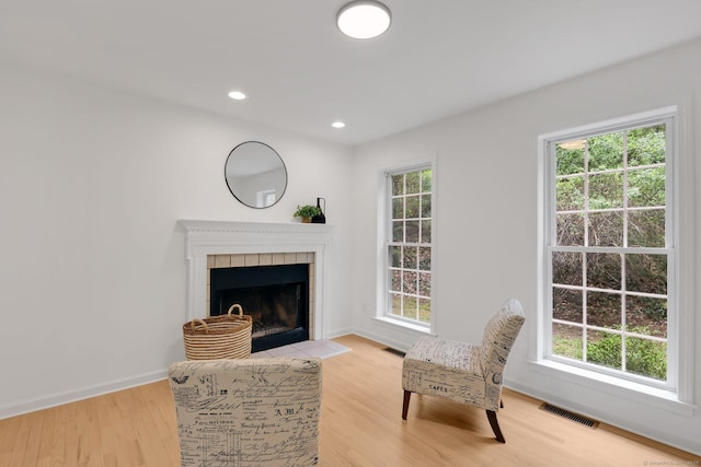 living area with plenty of natural light, light wood-type flooring, a tiled fireplace, and recessed lighting
