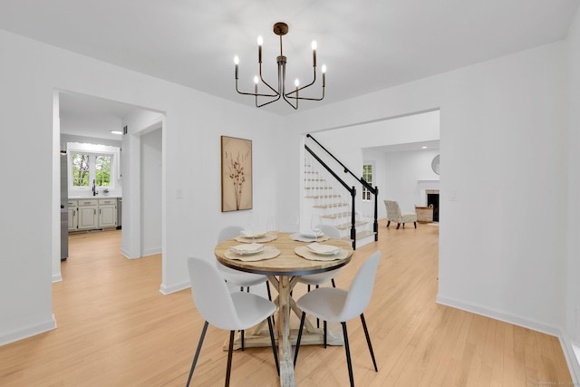 dining space featuring stairway, light wood-style flooring, a chandelier, and baseboards