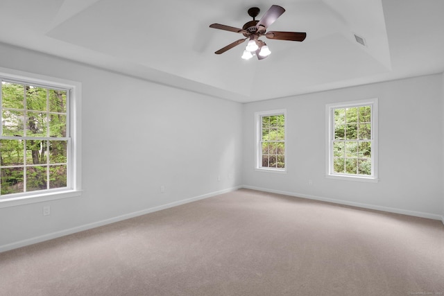 carpeted spare room featuring a tray ceiling and baseboards