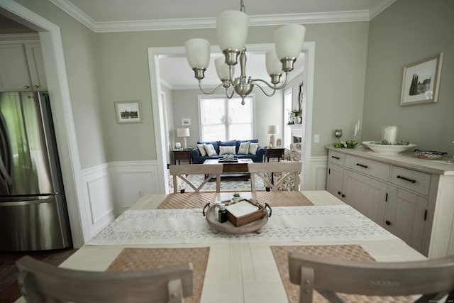 dining space with a chandelier, ornamental molding, a wainscoted wall, and a decorative wall
