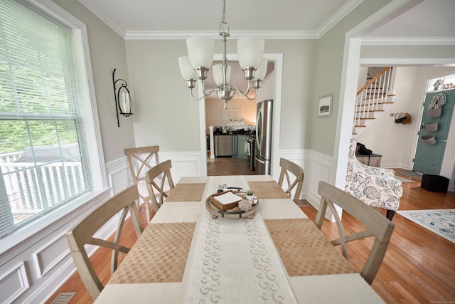 dining space with crown molding, a chandelier, wood finished floors, wainscoting, and stairway