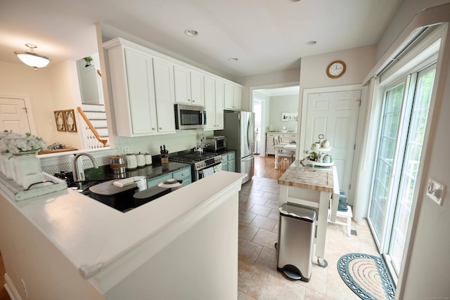 kitchen featuring appliances with stainless steel finishes, tasteful backsplash, white cabinets, a peninsula, and a sink
