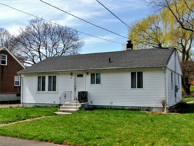 view of front facade featuring a chimney, a front yard, and roof with shingles