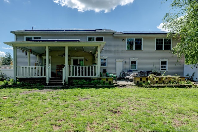 rear view of house featuring a ceiling fan, a lawn, roof mounted solar panels, and a patio