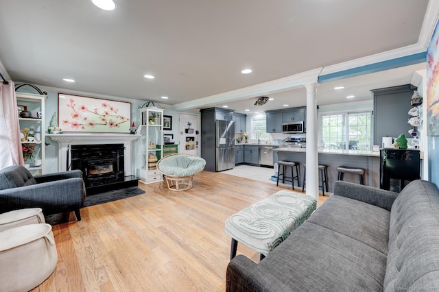 living room with crown molding, a glass covered fireplace, recessed lighting, light wood-style floors, and ornate columns