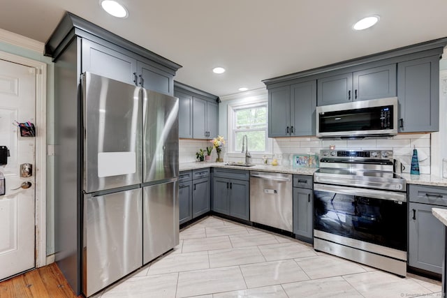 kitchen with appliances with stainless steel finishes, a sink, crown molding, light stone counters, and gray cabinets
