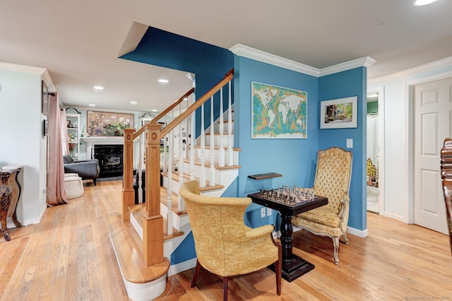 staircase with wood finished floors, a glass covered fireplace, recessed lighting, ornamental molding, and baseboards