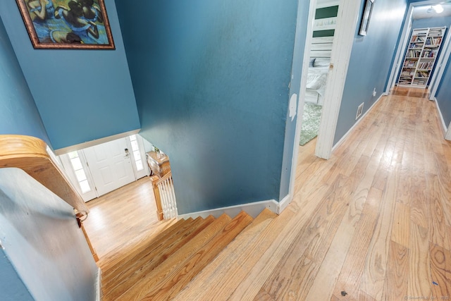 corridor featuring an upstairs landing, wood-type flooring, and baseboards