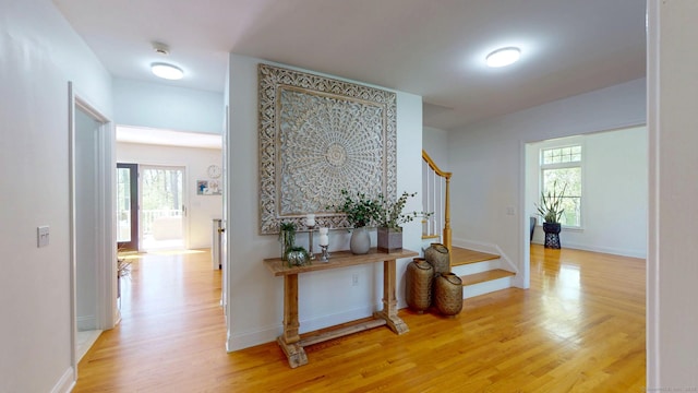 hall with stairs, light wood finished floors, healthy amount of natural light, and baseboards