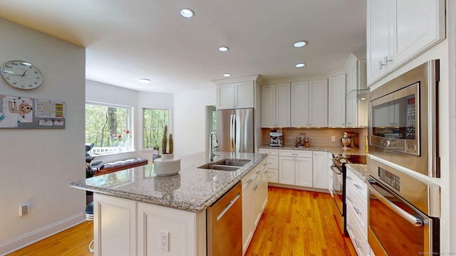 kitchen with stainless steel appliances, a sink, light wood finished floors, backsplash, and white cabinetry