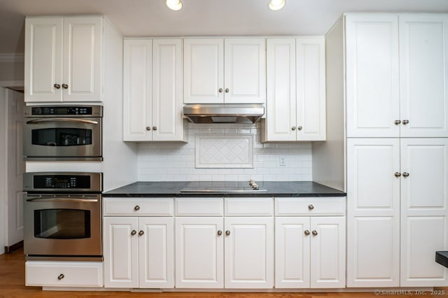 7 Indian Trl, Woodbridge, CT 06525 - kitchen with under cabinet range hood, black electric cooktop, white cabinetry, dark countertops, and decorative backsplash
