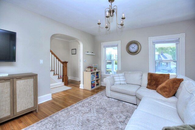 living room featuring wood finished floors, arched walkways, baseboards, stairway, and a chandelier