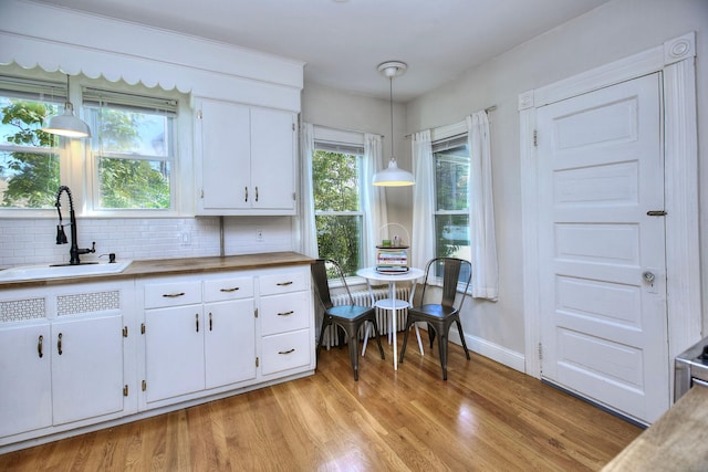 kitchen featuring a sink, radiator, light wood-type flooring, baseboards, and white cabinetry