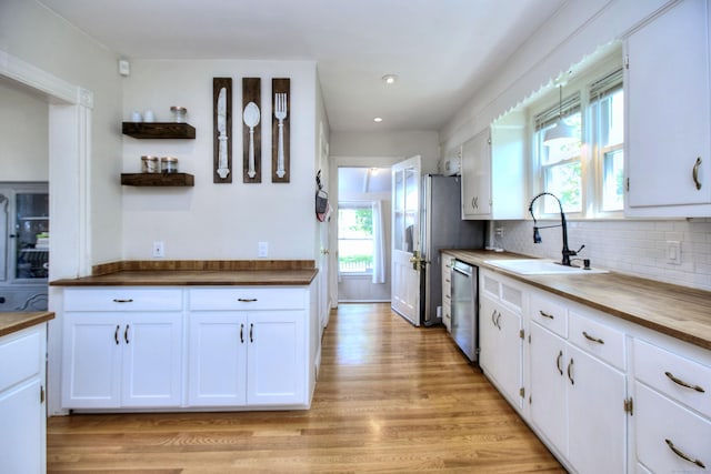 kitchen with a sink, stainless steel dishwasher, white cabinetry, light wood finished floors, and tasteful backsplash