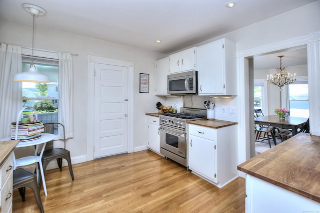 kitchen with appliances with stainless steel finishes, a chandelier, light wood-type flooring, decorative backsplash, and white cabinetry