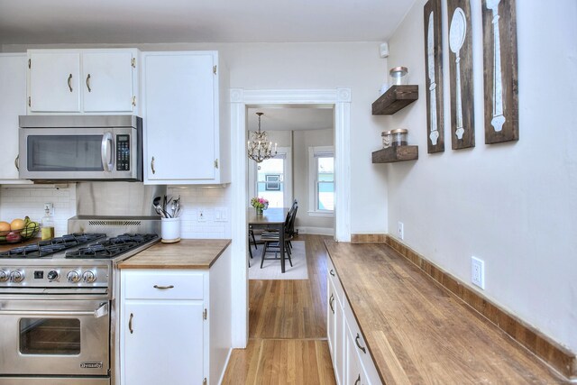kitchen with stainless steel appliances, butcher block countertops, a chandelier, decorative backsplash, and white cabinets