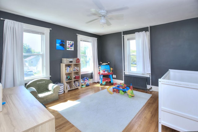 bedroom featuring radiator heating unit, wood finished floors, ceiling fan, and baseboards