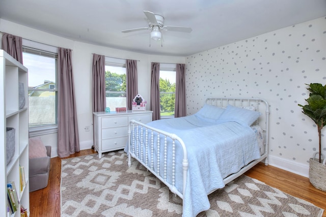 bedroom with light wood-type flooring, baseboards, wallpapered walls, and a ceiling fan