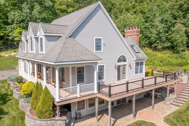 rear view of house featuring a shingled roof, a patio, a wooden deck, and a chimney