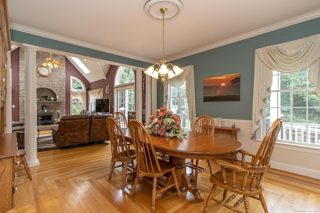 dining area with ornate columns, lofted ceiling, a chandelier, ornamental molding, and a large fireplace