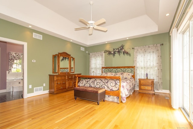 bedroom with a tray ceiling, wood finished floors, baseboards, recessed lighting, and ensuite bathroom