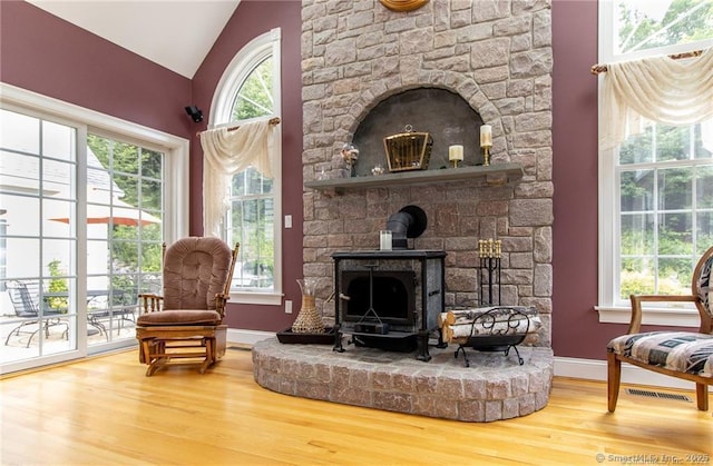 sitting room with wood finished floors, a wood stove, baseboards, and lofted ceiling