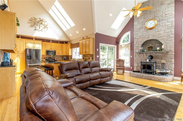 living area with light wood-style floors, a skylight, a ceiling fan, a wood stove, and high vaulted ceiling