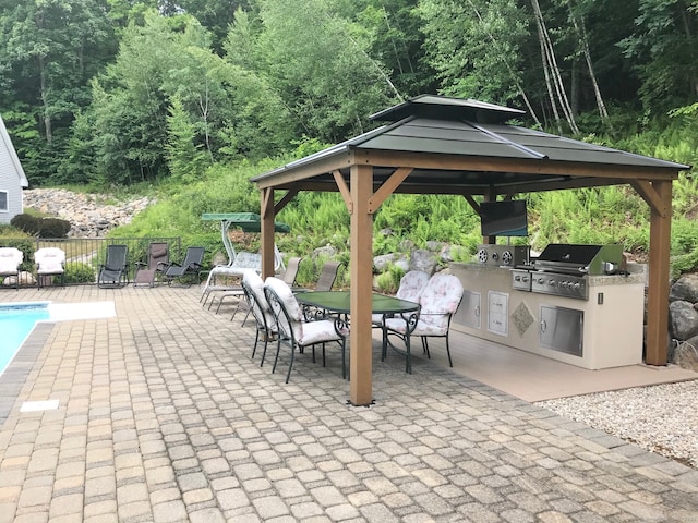 view of patio featuring a grill, a gazebo, an outdoor kitchen, outdoor dining area, and a wooded view