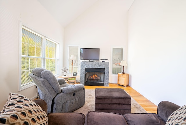 living room with wood finished floors, healthy amount of natural light, high vaulted ceiling, and a tiled fireplace