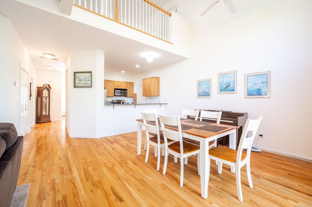 dining area featuring light wood-style floors, baseboards, a towering ceiling, and a ceiling fan